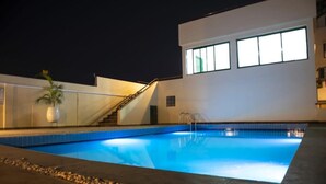 Una piscina con borde de piedra, una palmera y un edificio moderno con grandes ventanales.