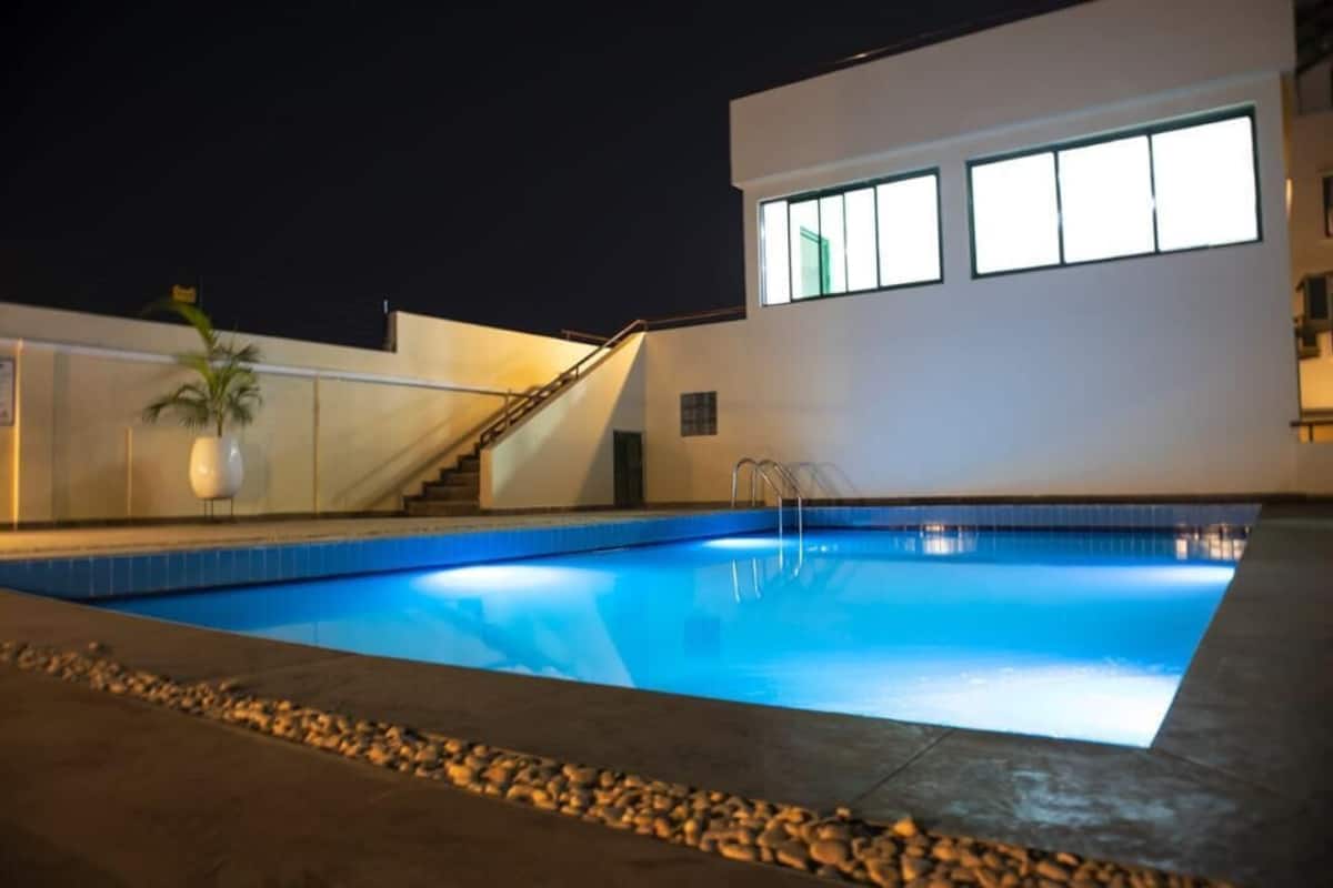 A swimming pool with a stone border, a palm tree, and a modern building with large windows.
