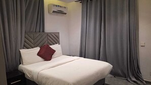 Una cama bien hecha con cabecera, cortinas grises y una mesita de noche con cajones.