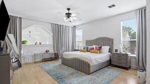 Une chambre à coucher comprenant un lit, des tables de chevet, un ventilateur de plafond, une fenêtre avec des stores et une vue sur l’extérieur.