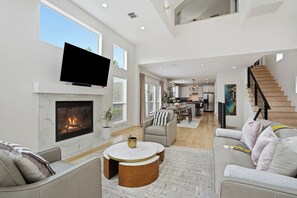Una sala de estar amplia con chimenea, televisor montado en la pared y una escalera que conduce a un nivel superior.