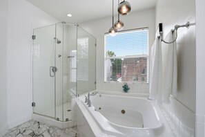 Un baño moderno con ducha envuelta en vidrio, una bañera amplia y una ventana con persianas.
