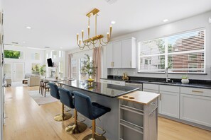 Una cocina moderna con una isla central, taburetes de bar y una lámpara de araña.
