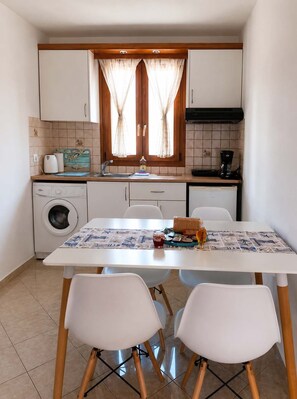 A compact kitchen with a washing machine, a coffee maker, and a dining table with chairs. - Island Flavor - Naxos Seaview Retreat With Balcony (Naxos)