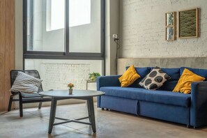 Ein Zimmer mit einem blauen Sofa, einem runden Tisch, einem Stuhl und einem großen Fenster.
