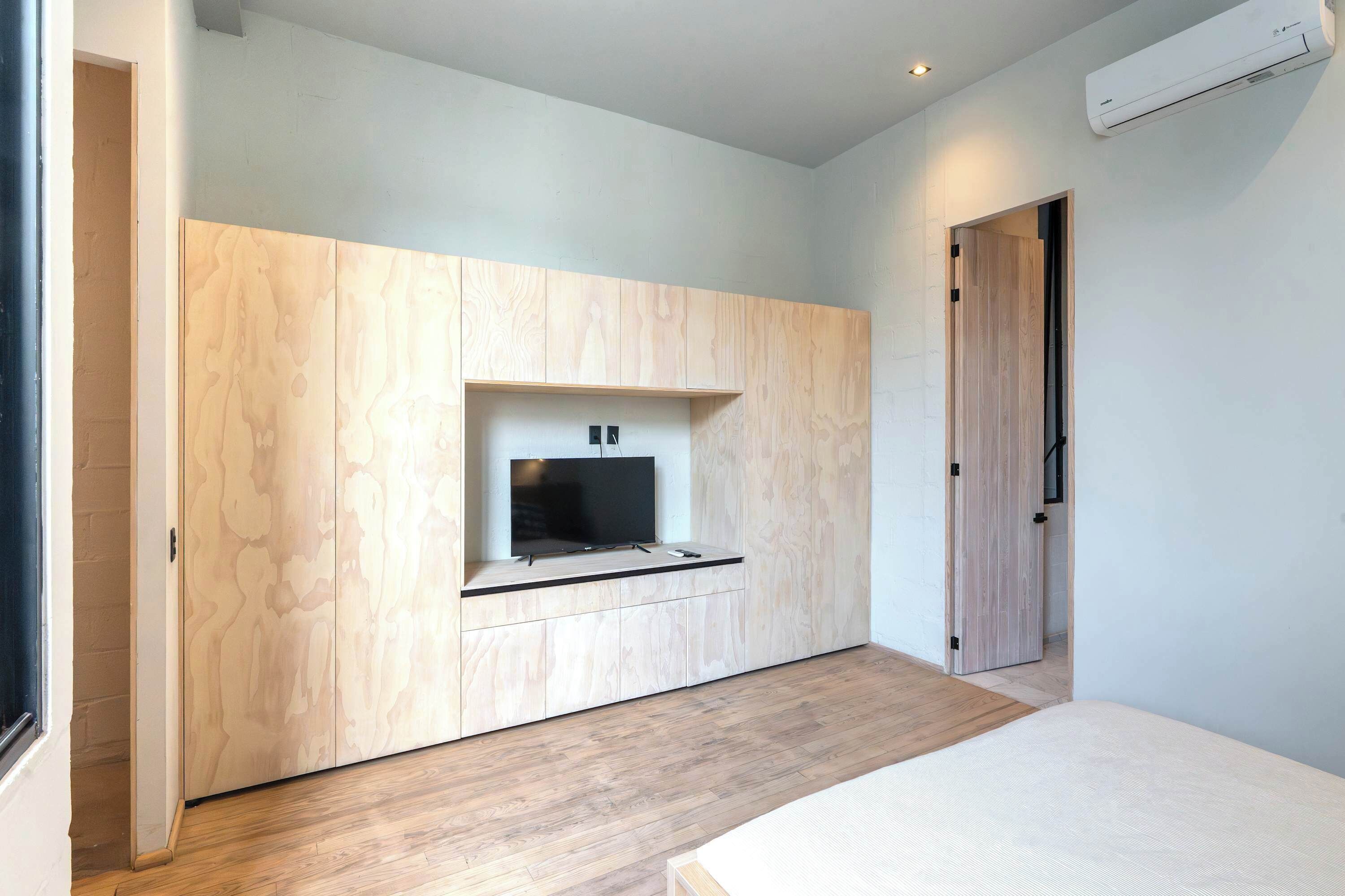 Una habitación moderna con televisión integrada, suelo de madera y una puerta que conduce a otra estancia.