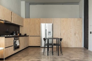 Eine moderne Küche mit Holzschränken, einem Edelstahlkühlschrank, einem Gasherd und einem Esstisch mit Stühlen.