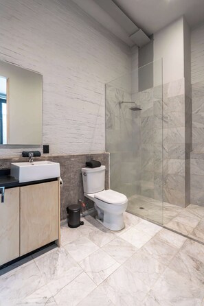 Ein modernes Badezimmer mit Marmorboden, Waschbecken, Toilette und einer Duschkabine aus Glas.