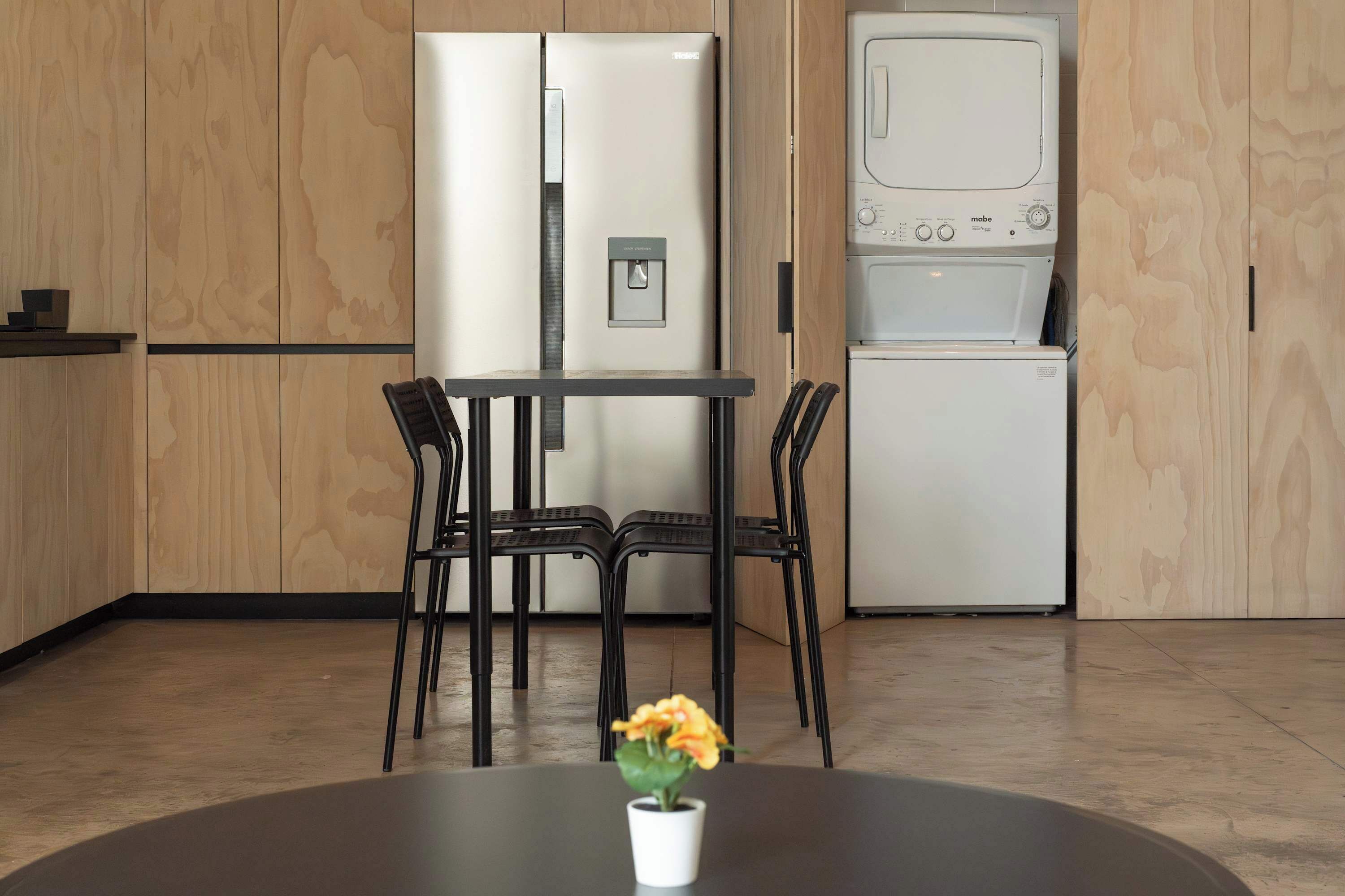 Cozinha moderna com frigorífico embutido, micro-ondas e máquina de lavar loiça. Há uma mesa de jantar com quatro cadeiras e uma planta num vaso sobre ela.