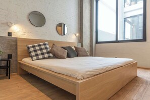 Ein modernes Schlafzimmer mit einem hölzernen Bett, zwei Wandspiegeln und einem großen Fenster.