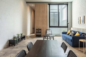 Ein modernes Wohnzimmer mit einem großen Fenster, einem blauen Sofa, einem Esstisch und schwarzen Stühlen.