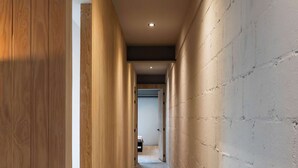 Un couloir avec un lambris en bois d’un côté et un mur en briques blanches de l’autre, qui mène à une pièce au bout.