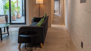 Un couloir avec un canapé, une table et une lampe. Des plantes en pot sont placées à l’extérieur, près de la fenêtre.