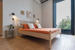 Een moderne slaapkamer met een houten bed, een klein nachtkastje met een plant en uitzicht door een groot raam.