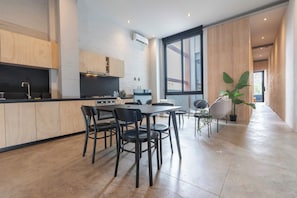 Eine moderne Küche mit Holzausbau, ein Essbereich mit Tisch und Stühlen und ein großes Fenster, das für natürliches Licht sorgt.