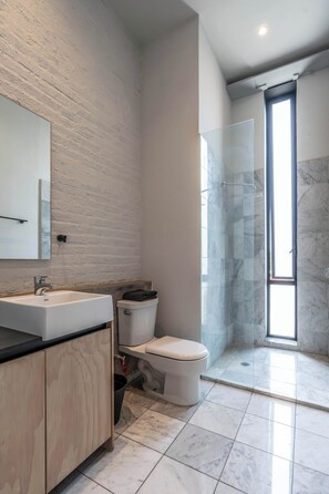 Een moderne badkamer met een douche van marmer, een wastafel met spiegel en een toilet.