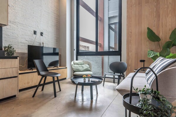 Een moderne woonkamer met een televisie, twee stoelen, een bank, een salontafel en een groot raam.