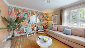 Ein Wohnzimmer mit einer Couch, Sesseln, einem Couchtisch, einer Zimmerpflanze und einer Wand mit einem Blattmuster.