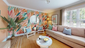 Ein Wohnzimmer mit einer Couch, Sesseln, einem Couchtisch, einer Zimmerpflanze und einer Wand mit einem Blattmuster.