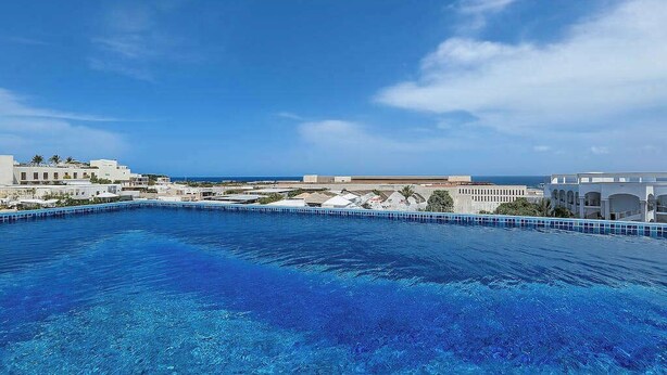En swimmingpool med utsikt över havet och byggnader i bakgrunden.
