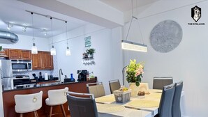 Eine moderne Küche mit Edelstahlgeräten, ein Essbereich mit weißem Tisch und schwarzen Stühlen sowie ein dekoratives Wandbild.