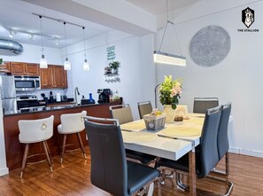 Eine moderne Küche mit Edelstahlgeräten, ein Essbereich mit weißem Tisch und schwarzen Stühlen sowie ein dekoratives Wandbild.
