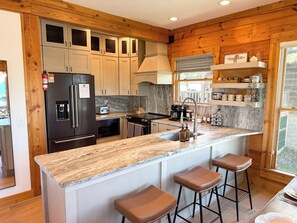 Una cocina con armarios de madera, un refrigerador, una estufa, un fregadero y taburetes de bar.