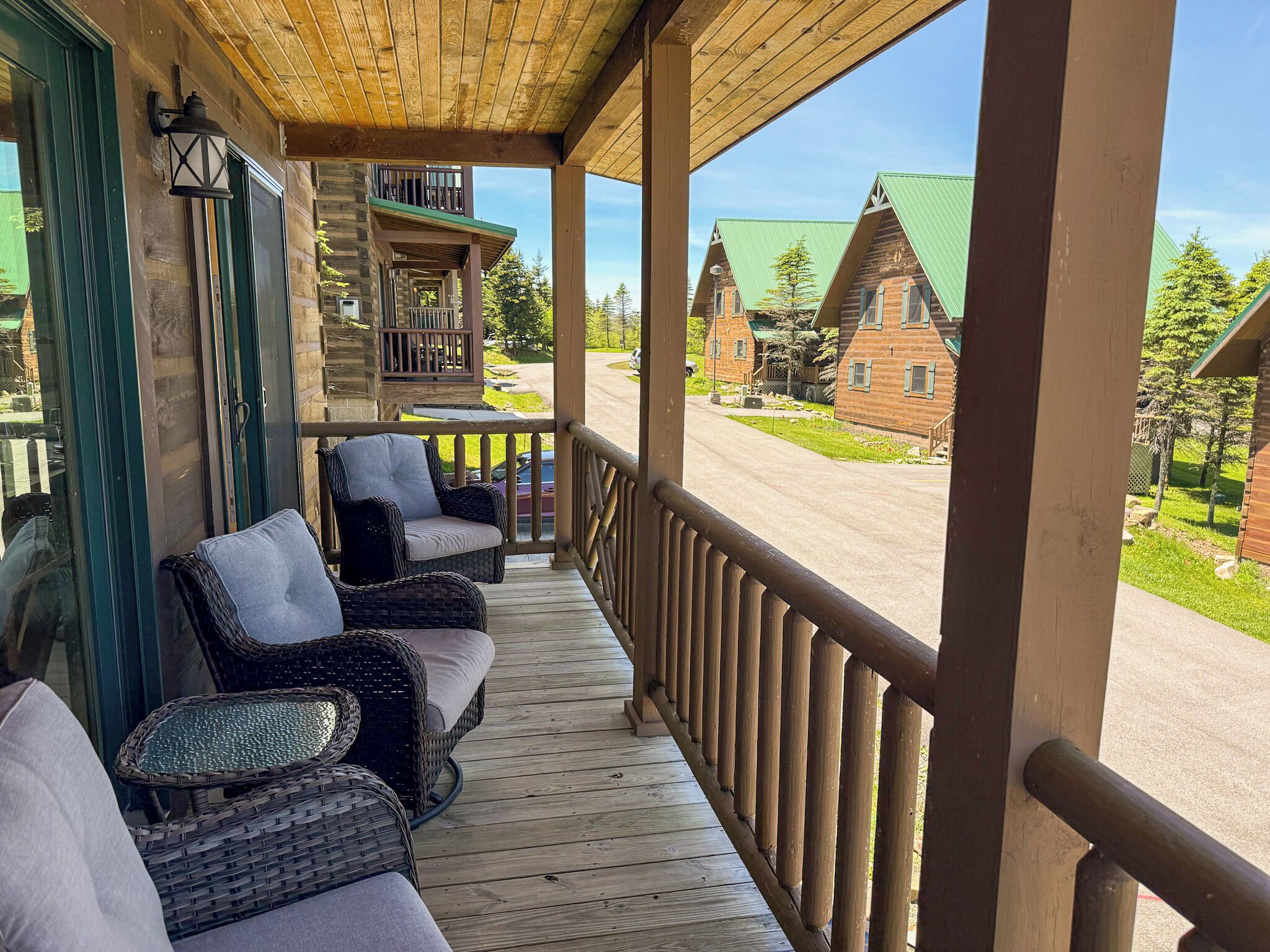A wooden porch with wicker furniture, a view of a street, and a building with a green roof.