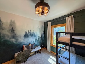 A bunk bed room with a forest mural, a window with curtains, and a hanging light fixture.