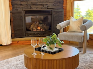 Una sala de estar acogedora con chimenea de piedra, una mesa redonda de madera, dos vasos y una planta en maceta.