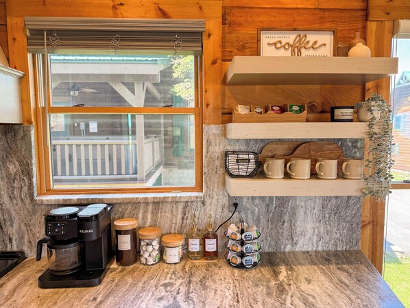 A kitchen with a coffee maker, jars of sugar and vanilla, and a mug rack.
