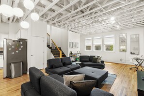 A modern living room with a sectional sofa, a staircase, and a kitchen area. - Luxury 2BR Condo on Peters St - Walk to FIFA & Mercedes-Benz Stadium (Atlanta)