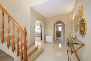 A modern interior with a wooden staircase, a glass table with golden legs, and a hallway leading to another room. - Newly Renovated Luxury Villa | Heated Pool, Rooftop & Outdoor Gym (javea)