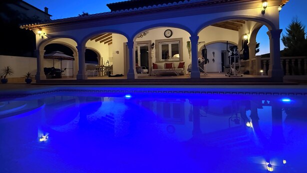 Una villa junto a la piscina con un porche cubierto, comedor y sala de estar.