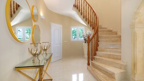 Un vestíbulo amplio con una escalera de mármol, una mesa de centro de cristal y un espejo grande.