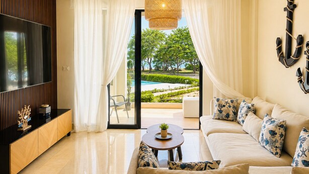 Una sala de estar moderna con sofá, televisor y vista a una piscina y follaje.