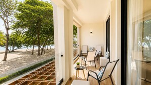 Un balcón con vistas a la playa, una zona de estar con sillas y una mesa, y suelo de madera.
