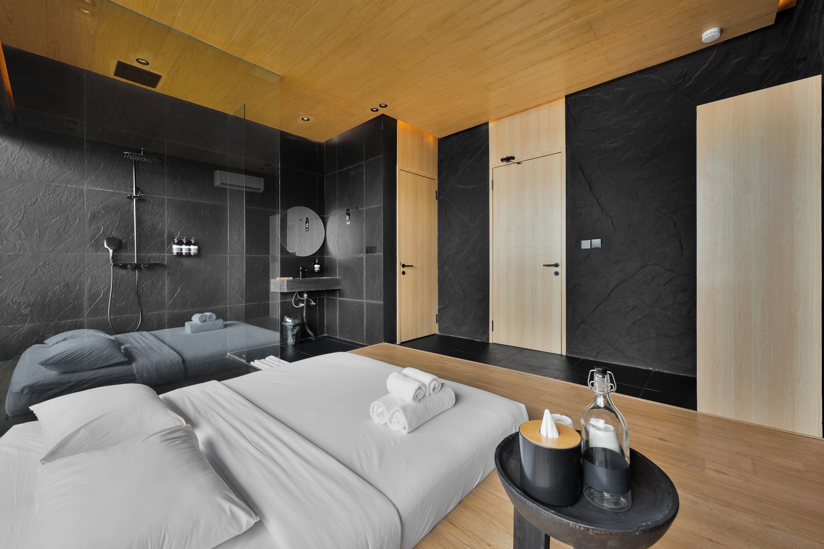 A modern hotel room with a large bed, a separate shower area, a vanity with a mirror, and a small table with toiletries.