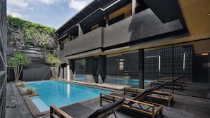 Un área de piscina moderna con sillones de descanso, una piscina cristalina y un edificio con fachada geométrica.