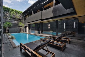 A modern pool area with lounge chairs, a clear pool, and a building with a geometric facade.