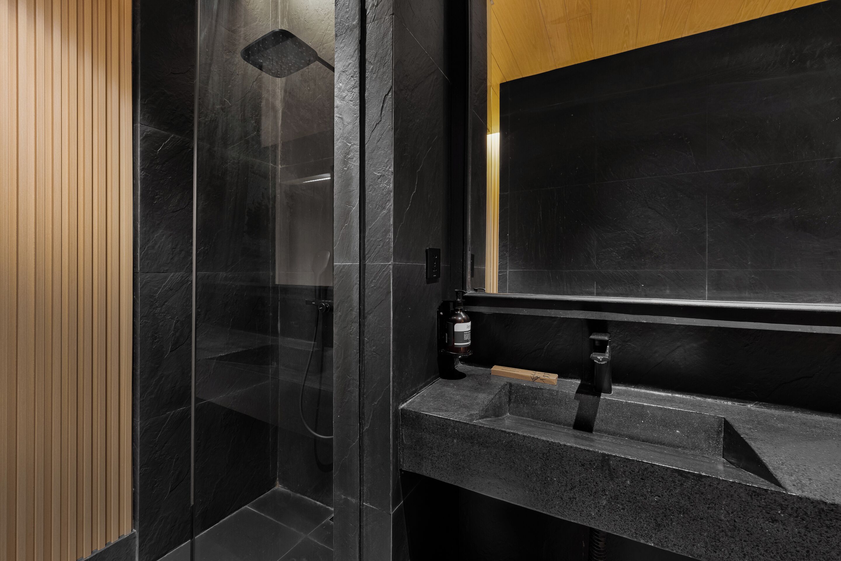 A modern bathroom with a glass shower enclosure, a wooden panel wall, and a granite countertop.