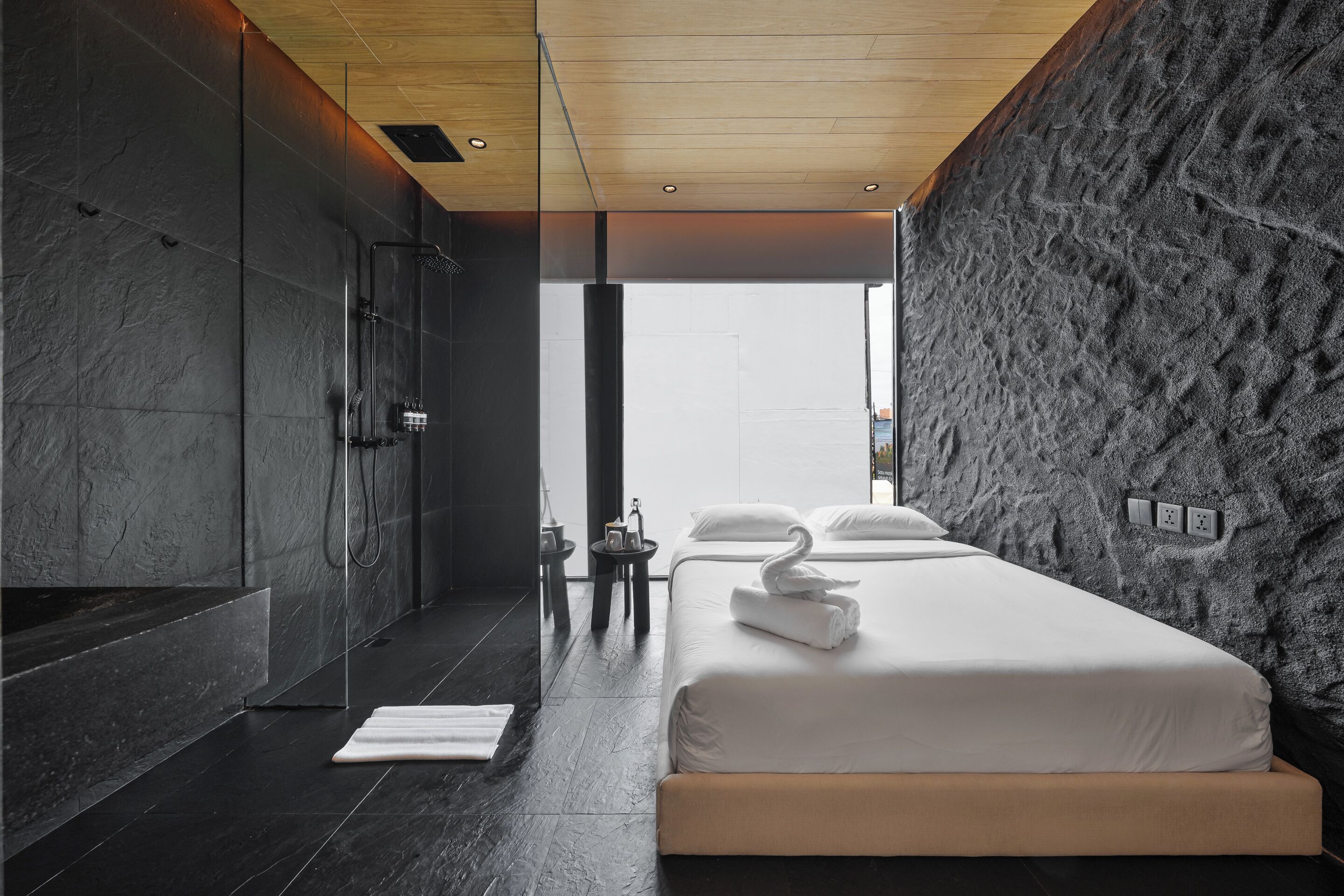 A modern bedroom with a large bed, a shower, and a view through a glass door.