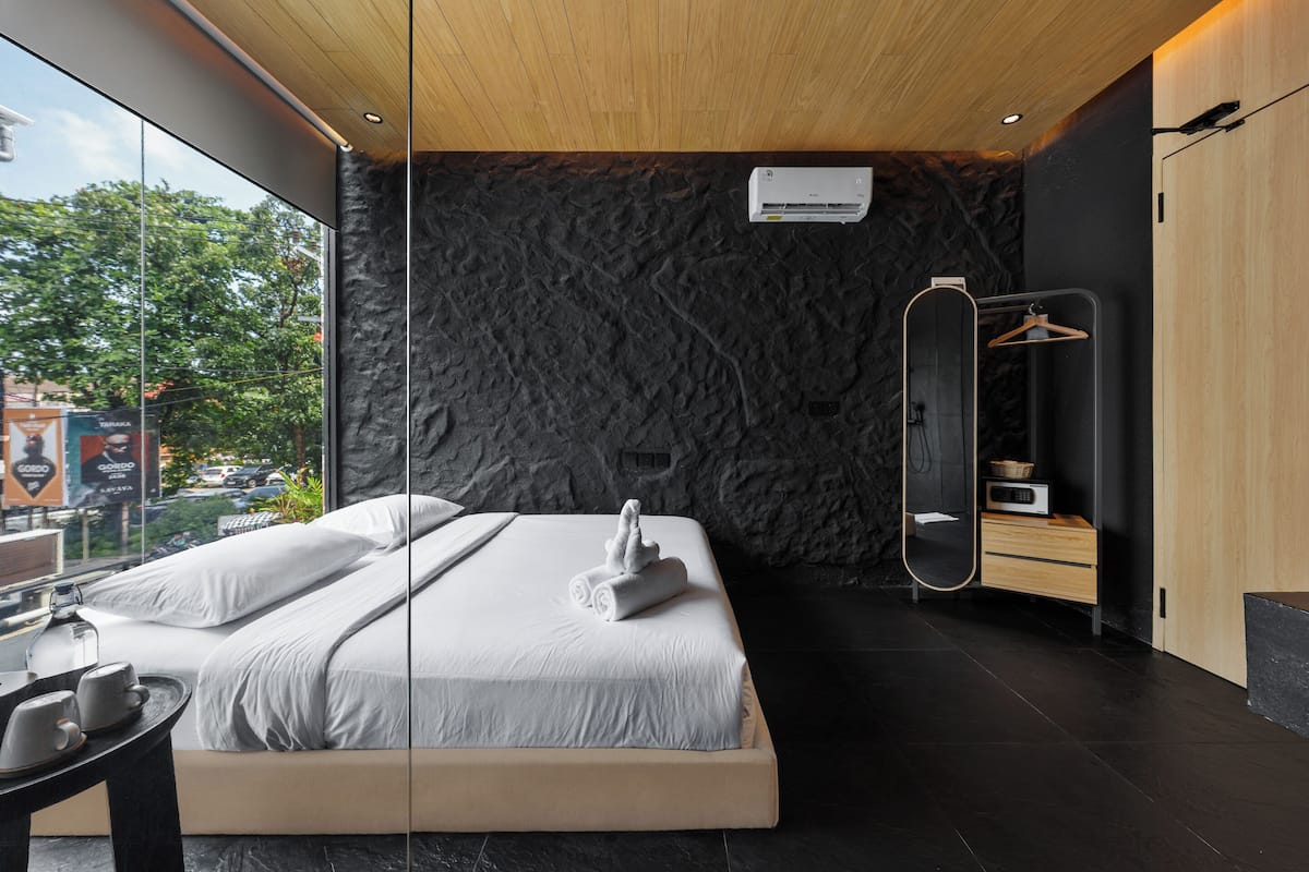Moderni hotellihuone, jossa on suuri sänky, puinen katto, kiviseinä, peili ja näkymä ulos.