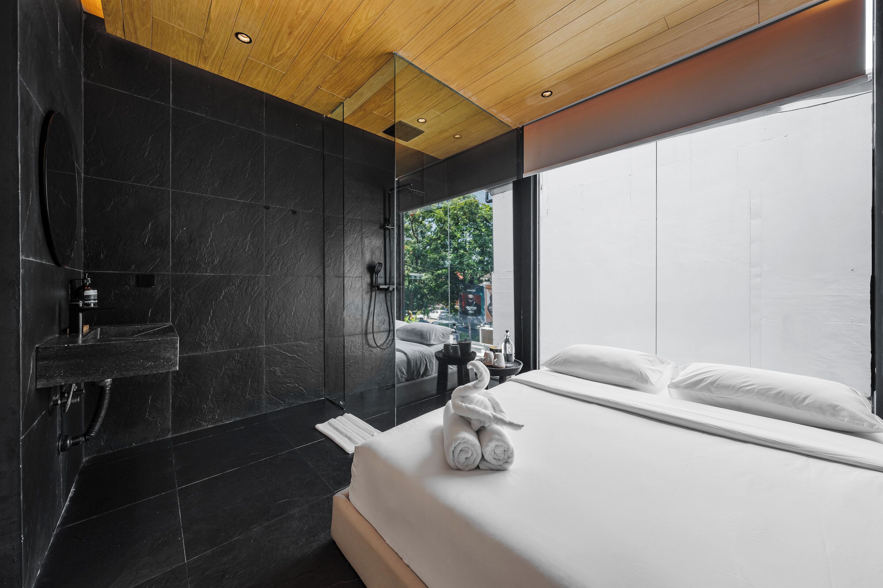 A modern hotel room with a large bed, a built-in shower, and a view through a large window.