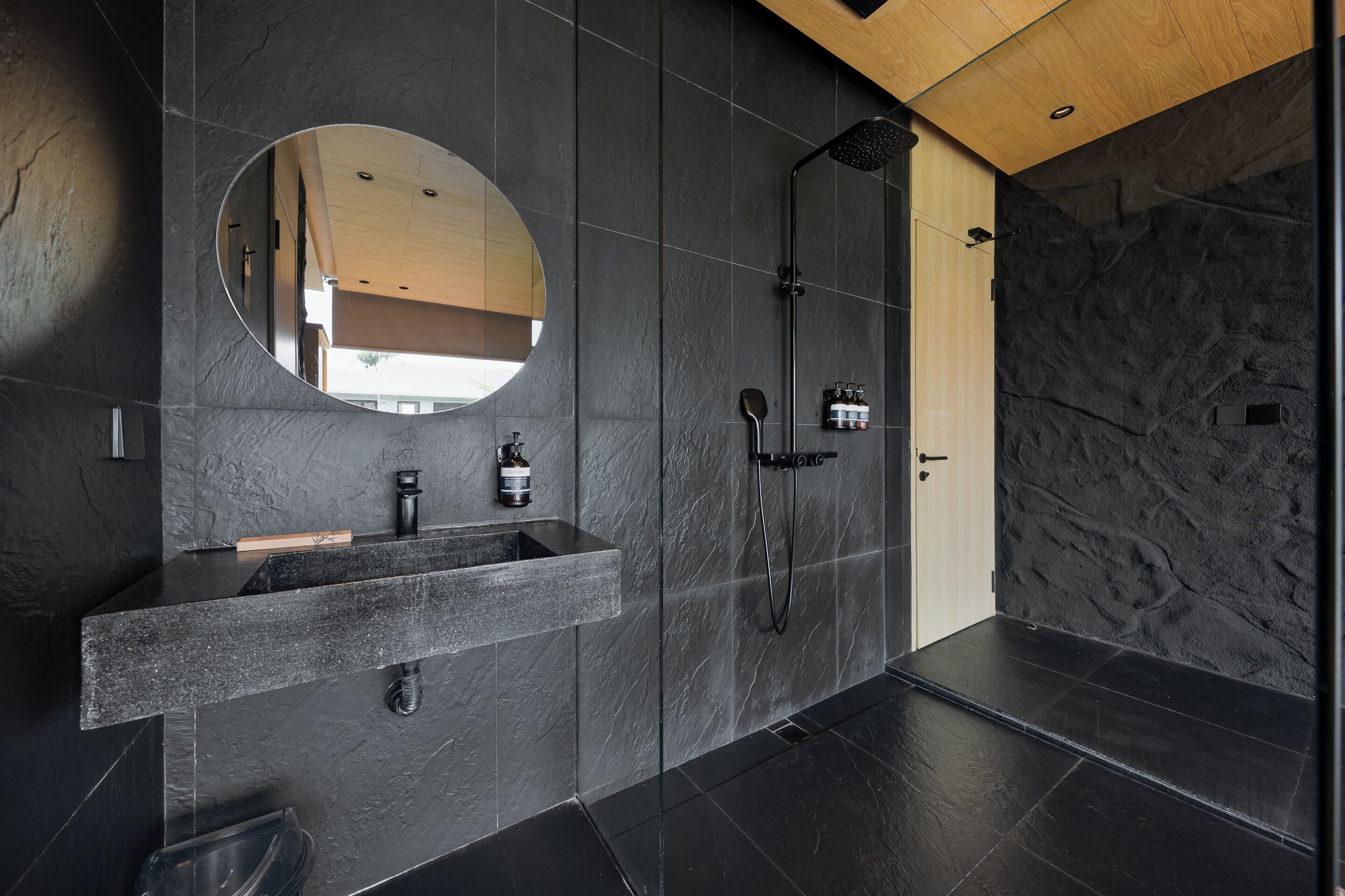 Une salle de bain moderne avec un grand miroir, un lavabo intégré, une douche et un mur à l’aspect pierre.