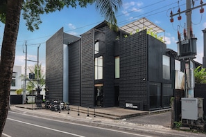 A modern building with a black facade, a visible entrance, and a sign reading 'M4YA BERHANWA'.