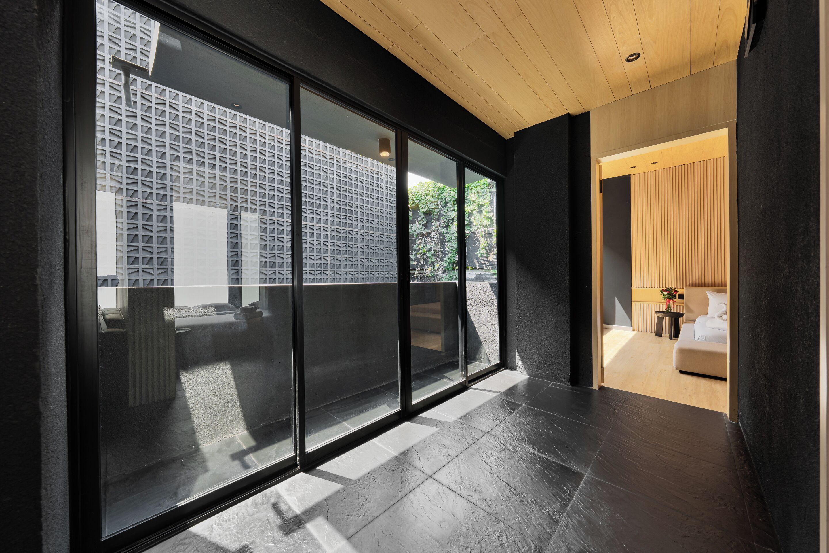 A modern interior with large sliding glass doors, a wooden ceiling, and a view of an outdoor area with a patterned wall.