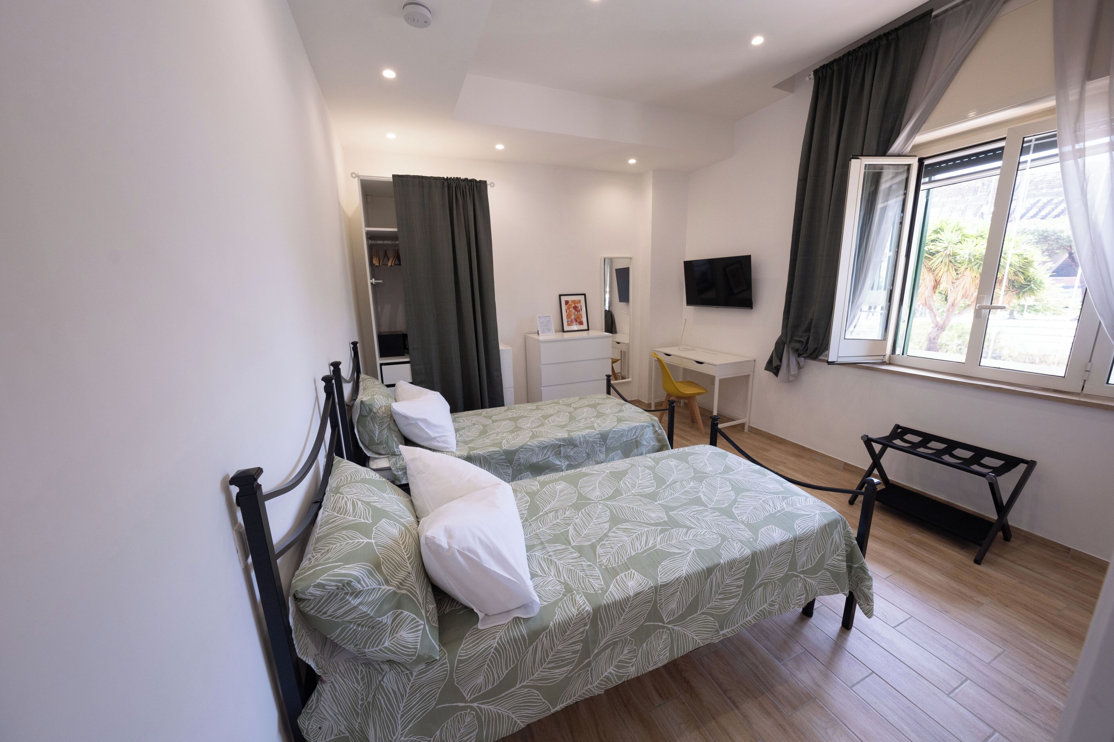 A hotel room with two beds, a desk, a chair, a TV, and a window with curtains.