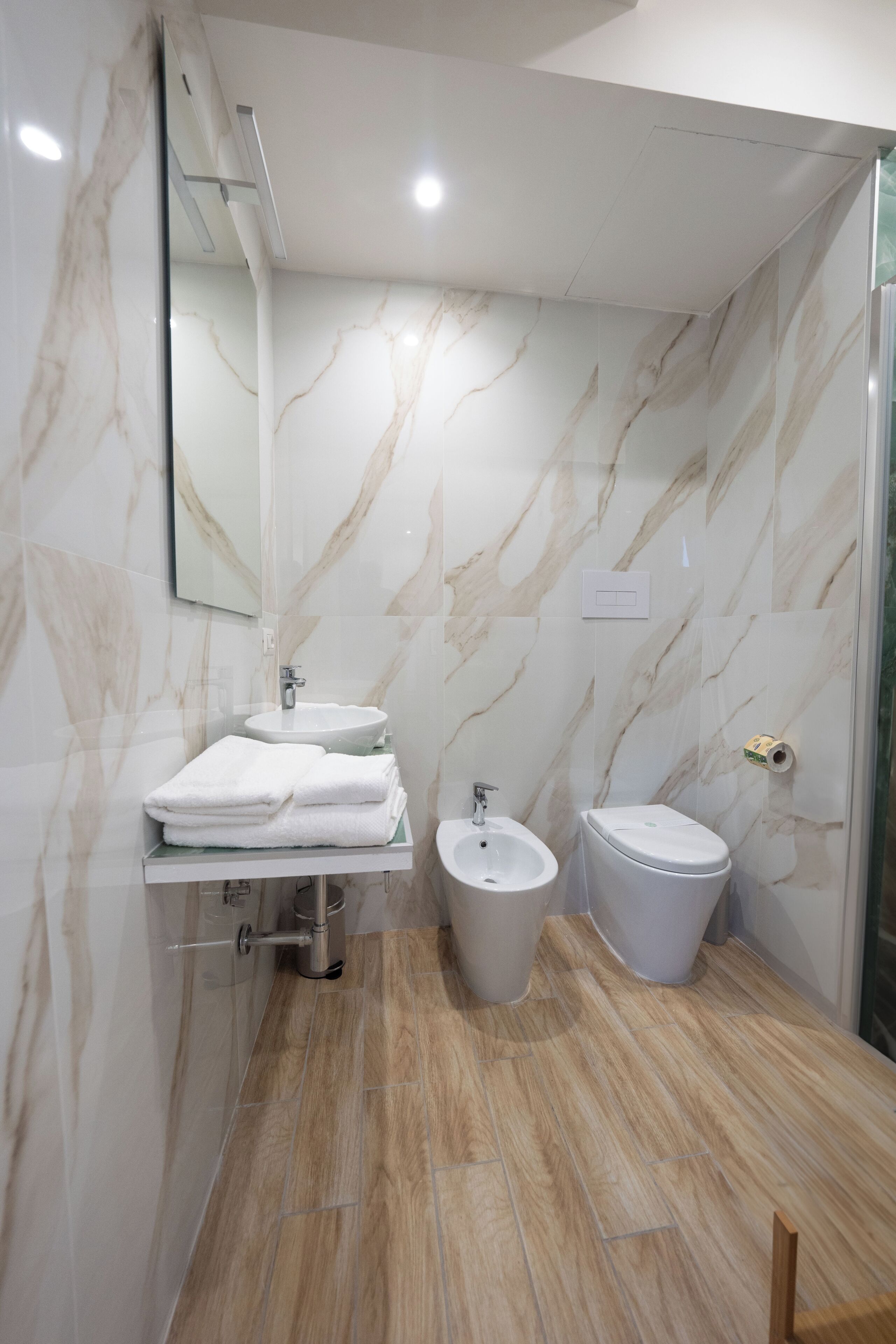 A bathroom with a marble wall, a sink, a bidet, and a toilet.