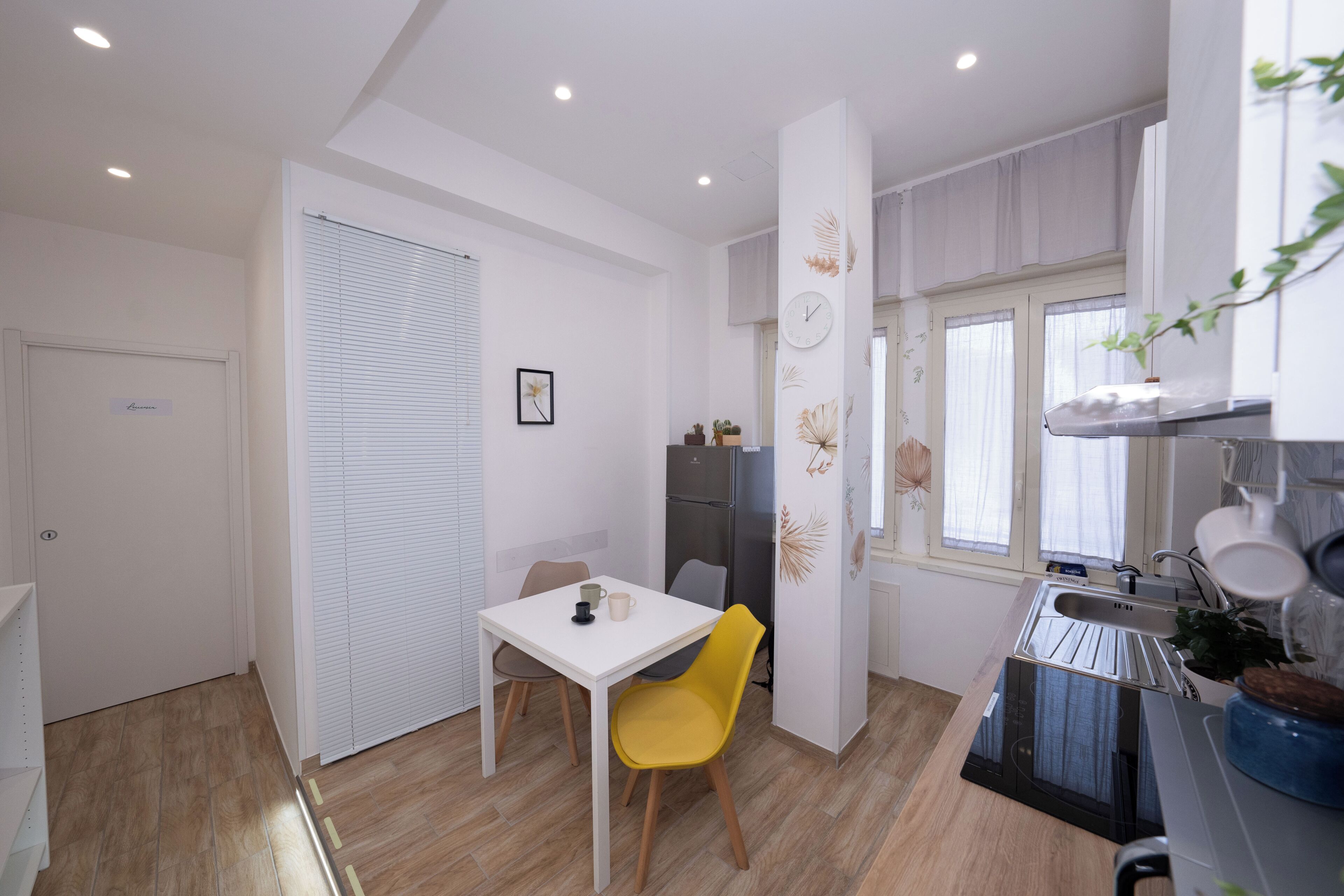 A compact kitchen with a white table and yellow chair, a refrigerator, and a sink.